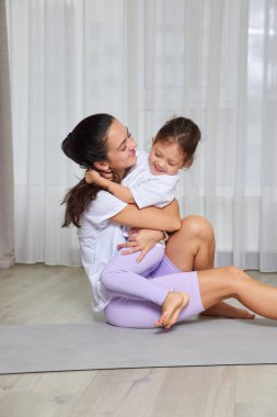 Yoga minderinde spor yaparken gülümseyen kızını kucaklayan mutlu bir anne.