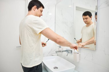 Genç adam modern bir banyoda diş fırçasıyla dişini fırçaladı.