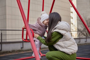 Anne, kızı şehir parkında salıncakta sallıyor.