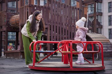 Anne ve kızı bir şehir parkında atlıkarıncada birlikte oynuyorlar.