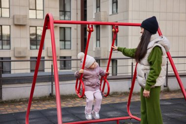 Anne kızını dışarıda salıncakta sallıyor.