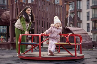 Anne ve kızı bir şehir parkında atlıkarıncada birlikte oynuyorlar.