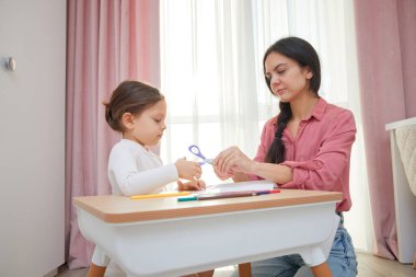 Anne ve kızı bir sanat projesi için makasla kağıttan tasarımlar kesiyorlar.