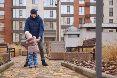 Baba küçük kızının ellerini tutuyor, onunla dışarıda oynuyor.