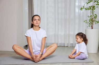 Anne ve kızı oturma odalarındaki paspasın üzerinde yoga yapıyor.