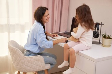 Kadın ve çocuk bir masayı paylaşıyor, uzaktan çalışma sırasında dizüstü bilgisayar ve deftere odaklanıyor