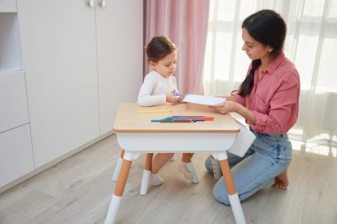 Anne ve kızı bir sanat projesi için makasla kağıttan tasarımlar kesiyorlar.