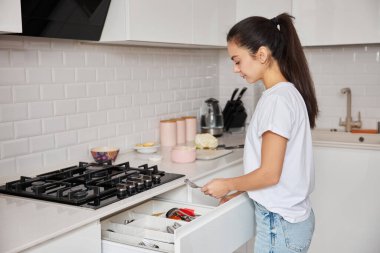 Modern mutfağını düzenleyen, yemek hazırladıktan sonra ortalığı toparlayan bir kadın.