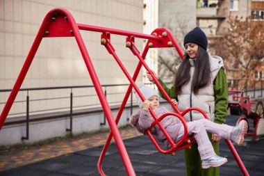 Anne kızını dışarıda salıncakta sallıyor.