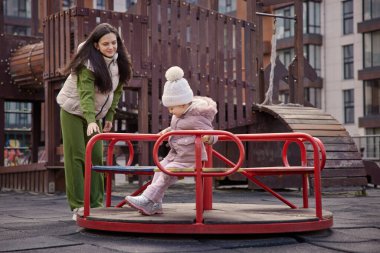 Anne ve kızı bir şehir parkında atlıkarıncada birlikte oynuyorlar.