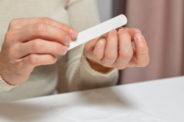 Kadın evde manikür yapıyor, tırnaklarını törpülüyor.