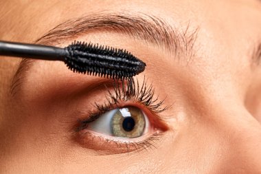 Kadının kirpiklerine rimel sürmesi, göz güzelliğini ve kozmetik ürünlerini vurgulaması.