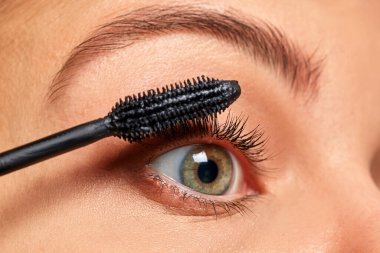 Kadının kirpiklerine rimel sürmesi, göz güzelliğini ve kozmetik ürünlerini vurgulaması.