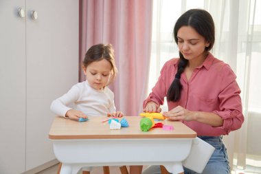 Anne ve kızı küçük bir masada renkli oyun hamuruyla oynuyorlar.