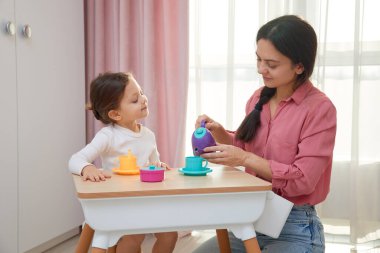 Anne ve kızı renkli oyuncaklarla çay partisi yapıyorlar.