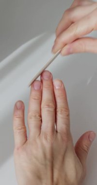 Beyaz bir masada manikür için tırnak törpüsü kullanan bir kadının elleri.