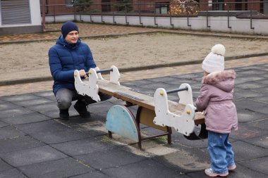 Baba ve küçük kızı kışın açık havada tahterevalli sürüşünün keyfini çıkarıyorlar.