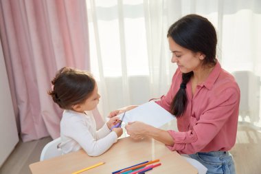 Anne ve kızı bir sanat projesi için makasla kağıttan tasarımlar kesiyorlar.
