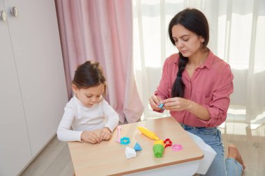 Anne ve kızı küçük bir masada renkli oyun hamuruyla oynuyorlar.