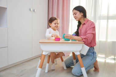 Anne ve kızı renkli oyuncaklarla çay partisi yapıyorlar.