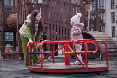 Anne ve kızı bir şehir parkında atlıkarıncada birlikte oynuyorlar.