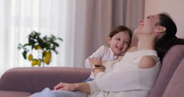 Anne ve kızının birbirini gıdıkladığı ve kanepede gülüp eğlendiği sevgi dolu bir aile anı.