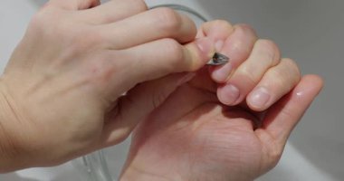 Beyaz arka planda bir kase su üzerinde meme uçlarıyla tırnak etlerini kesen bir kadının ellerini kapat.