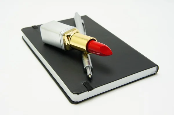 Lipstick and pen on a black notebook — Stock Photo, Image