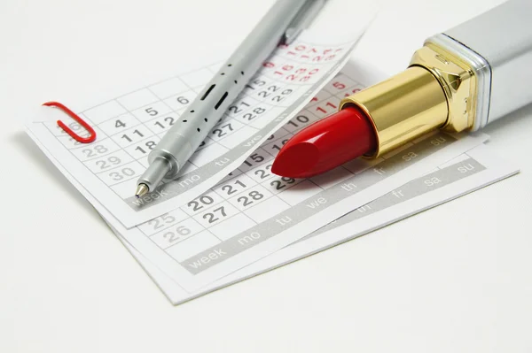 Lipstick and pen on calendar sheets — Stock Photo, Image