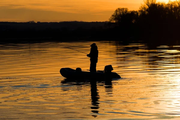 Un pescador en un barco caña de pescar al atardecer —  Fotos de Stock