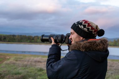 Çekici ve genç bir fotoğrafçının vahşi doğanın ortasında kameranın yakınlaştırıcı lensinden baktığı fotoğraf. Kış kıyafetleri giyiyordu. Kâşif, hayvan arıyor.