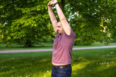 Parkta kolları gökyüzüne kadar uzanan ve gözleri kapalı genç ve çekici bir adamın fotoğrafı. Bir yaz günü doğada tek başına. Yoga pozu