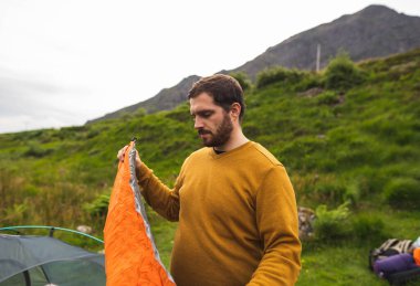 Genç ve çekici bir adam İskoçya 'da tek başına kamp yapmak için çadırının yanındaki yatağı şişiriyor. Tatil sırasında seyahat etmek için gerekli ekipman