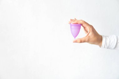 Beyaz arkaplanlı, âdet bardağı tutan genç bir kadın.