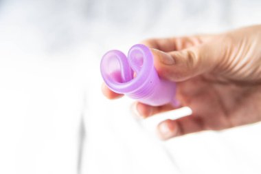 Beyaz arkaplanlı, âdet bardağı tutan genç bir kadın.