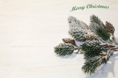 Dekoratif karla kaplı ladin dalları hafif ahşap bir arka planda yatar. Yazıtın üstünde: 