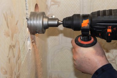The man makes holes in the wall with a drill. clipart
