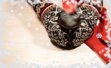 Parlak eldivenli iki el beyaz arka planda dumanı tüten bir fincan kahve tutuyor. Yakınlarda kırmızı bir eşarp var. Kar tanelerinin etrafında.