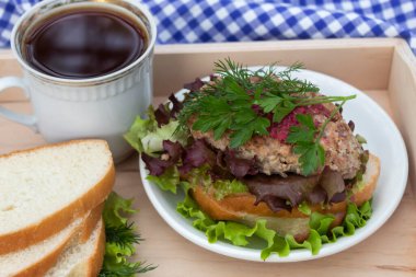 Tepside bir fincan kahve var. Yakınlarda bir tabak sandviç ve otlu ekmek var.. 