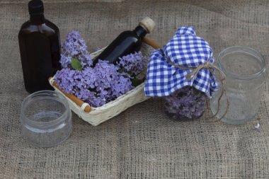 Masada şişeler, kavanozlar, bir sepet leylak çiçeği ve alkol dolu bir kavanoz leylak var..