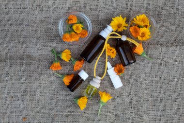 Calendula çiçekleri, şişeler ve yağ jüt kumaşın üzerinde bulunur..