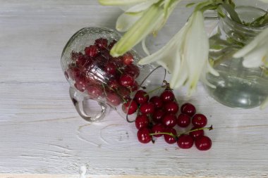 Yukarıdan bak. Beyaz arka planda, bir sürahi dağınık kiraz ve bir buket beyaz zambak..