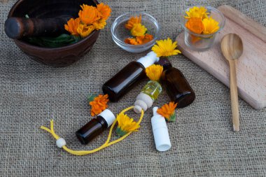 Masanın üzerinde takvim çiçekleri, bir kase, şişeler, kesme tahtası ve yağ var..