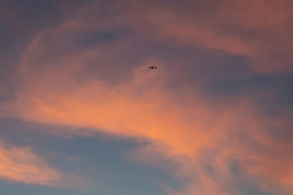 夕阳西下 云彩泛起红晕 在粉色云彩的背景下可以看到一架飞行的飞机 — 图库照片