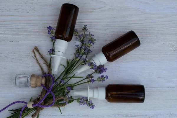 Lavender flowers, a bottle of oil and several bottles lie on a white wooden background.