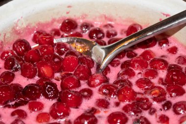 Yakın plan. Parlak kırmızı kirazlar bir kasede şeker şurubunda kaynatılır ve büyük bir kaşıkla karıştırılır..