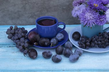 Hayat mavi tonlarda. Bardakta bir buket mavi aster var. Yanında fesleğenli bir fincan çay, bir demet üzüm ve mavi erik var..