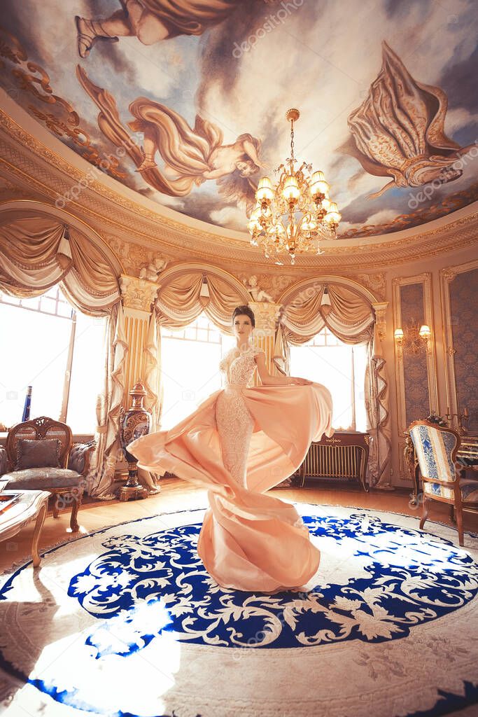 A beautiful young girl in a powdery wedding dress on the background of the interiors of a luxurious historical apartment. An elegant and stylish bride's morning.