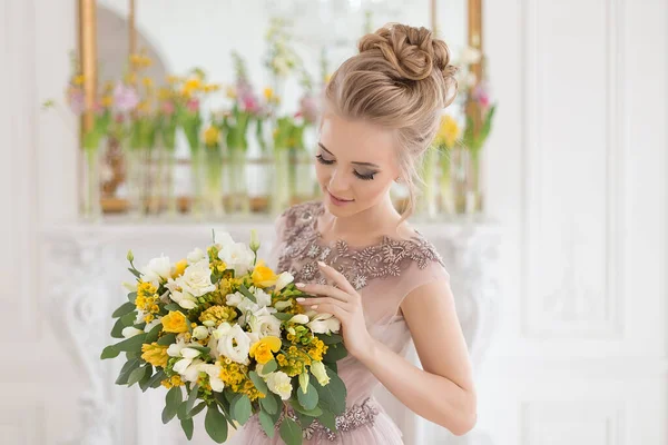 Bahar çiçekleriyle süslenmiş, arka planında bir buket sarı ve beyaz çiçekli bej renkli bir elbise içinde güzel, genç bir gelin. Kapalı alanda zarif bir düğün töreni..
