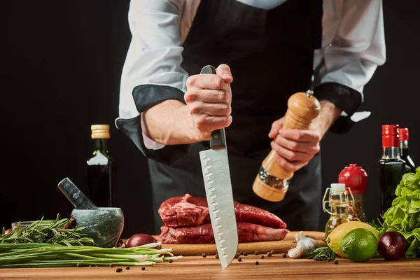 Gekke chef-kok die biefstuk kookt. De man stak zijn mes in tafel terwijl hij vlees peperde. — Stockfoto
